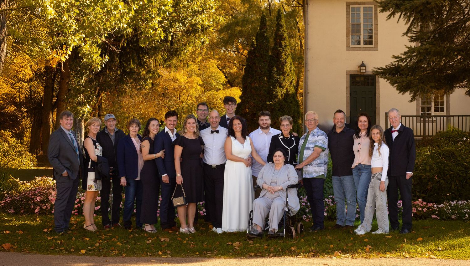 Wedding party group photo with bride and groom surrounded by family in an autumn garden setting.