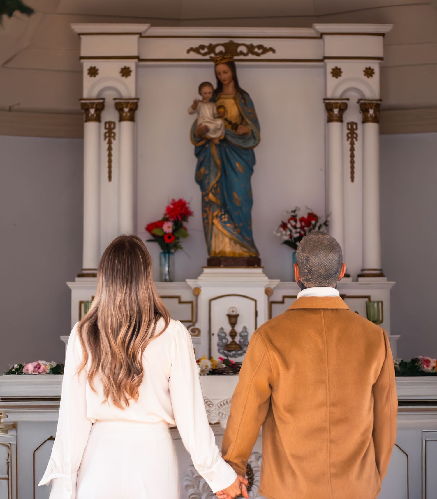 Couple holding hands facing a religious altar with Virgin Mary statue in a white chapel.