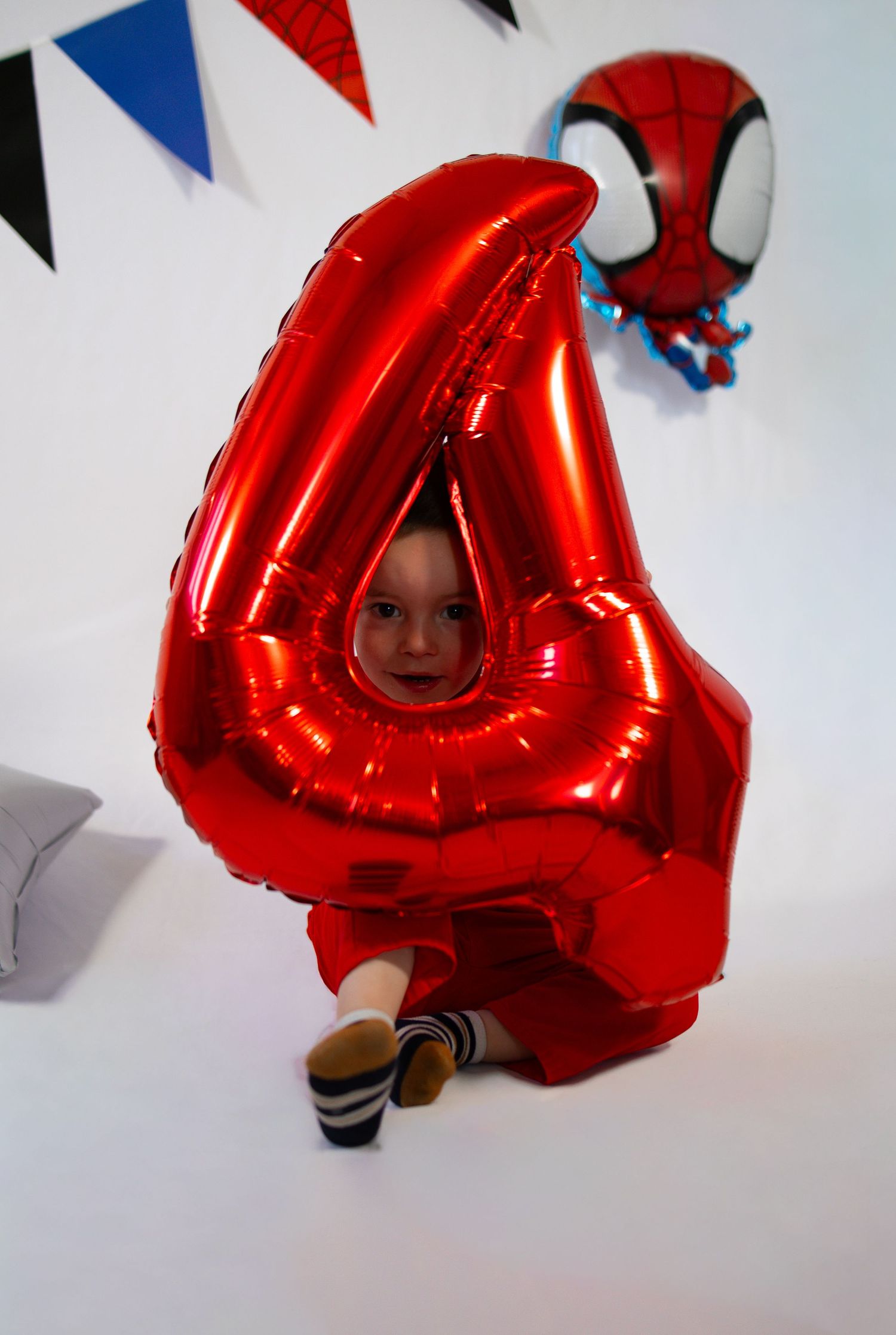 A child peeks through a large red number 4 foil balloon at a Spiderman birthday party.