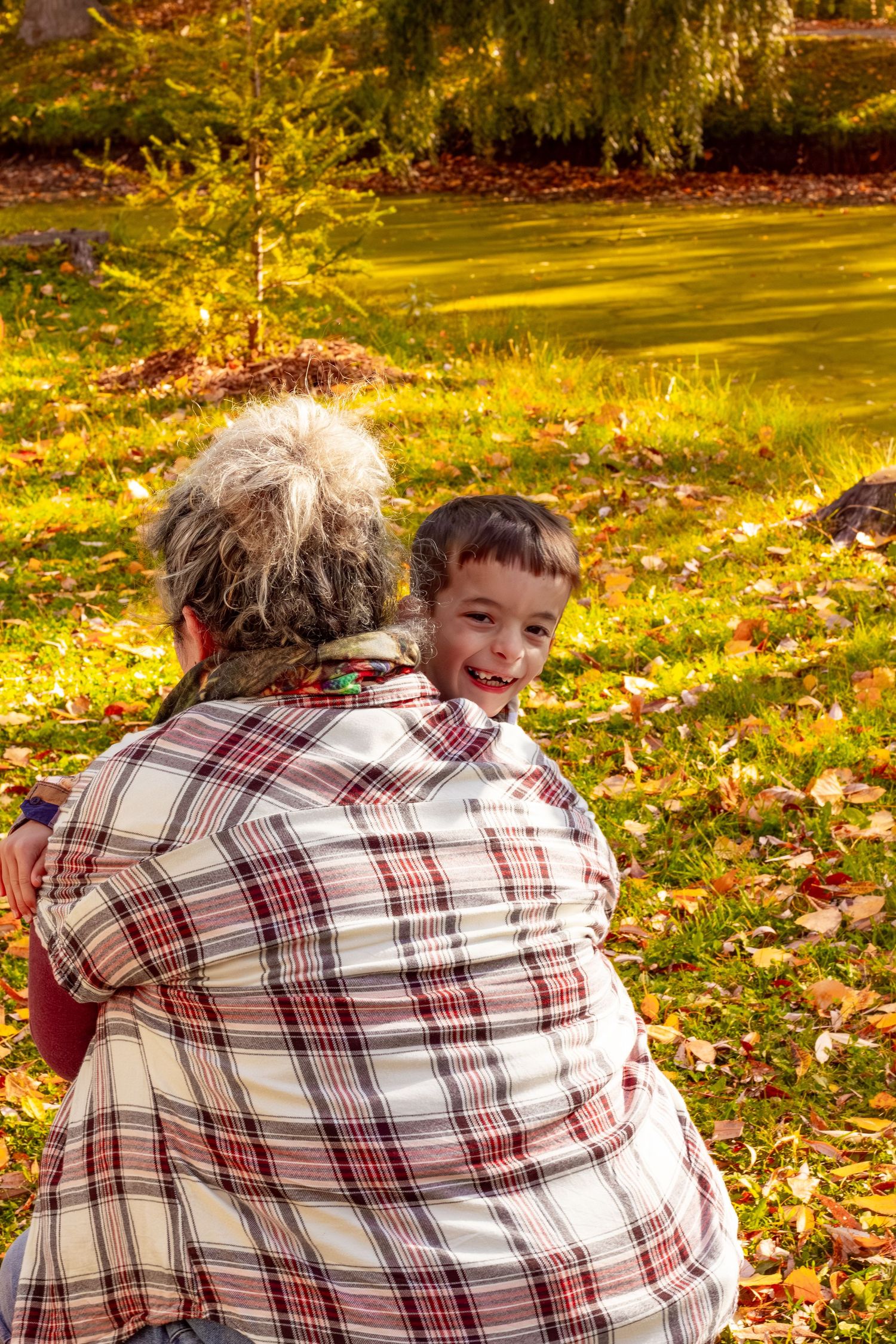 Grandmother hugging smiling young boy in a sunny autumn park with golden foliage background.