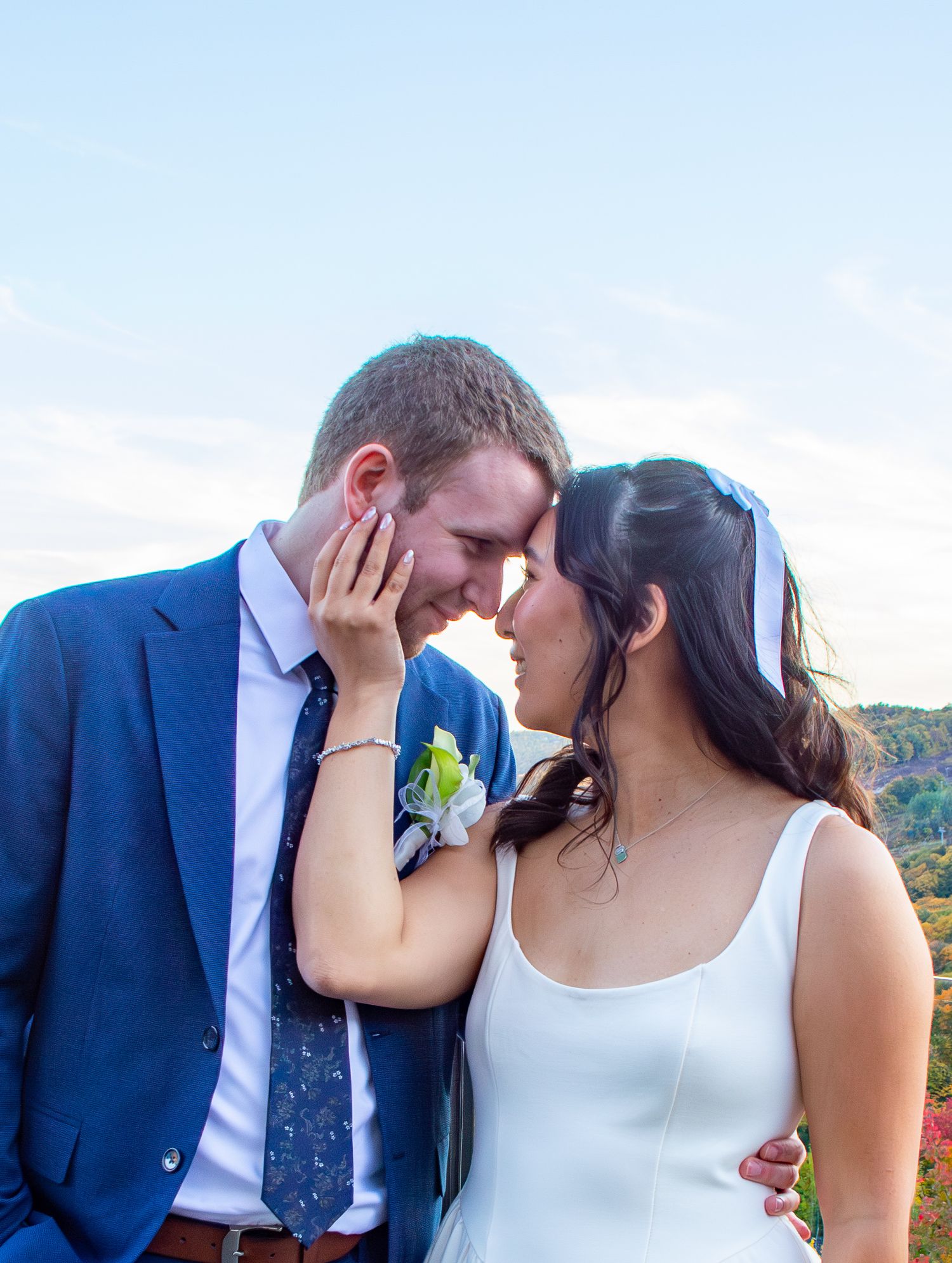 Newlywed couple sharing an intimate forehead touch against a scenic sky backdrop.