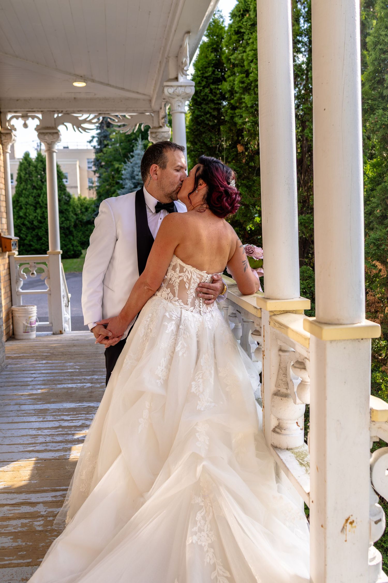Bride and groom sharing a romantic kiss on an elegant white columned porch, bride wearing a stunning lace ballgown.