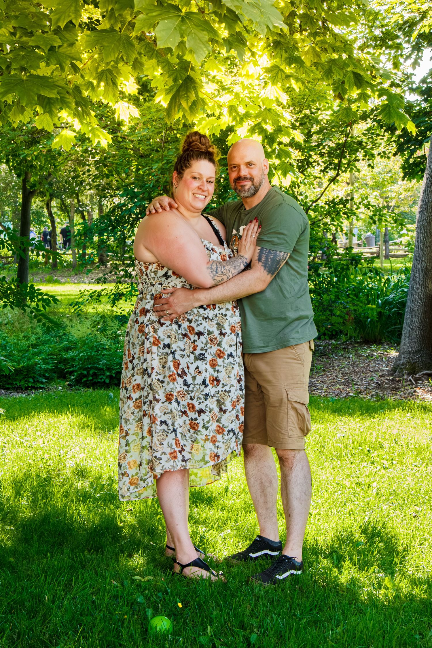 Couple souriant enlacé debout sous les arbres lors d'une séance photo en plein air.