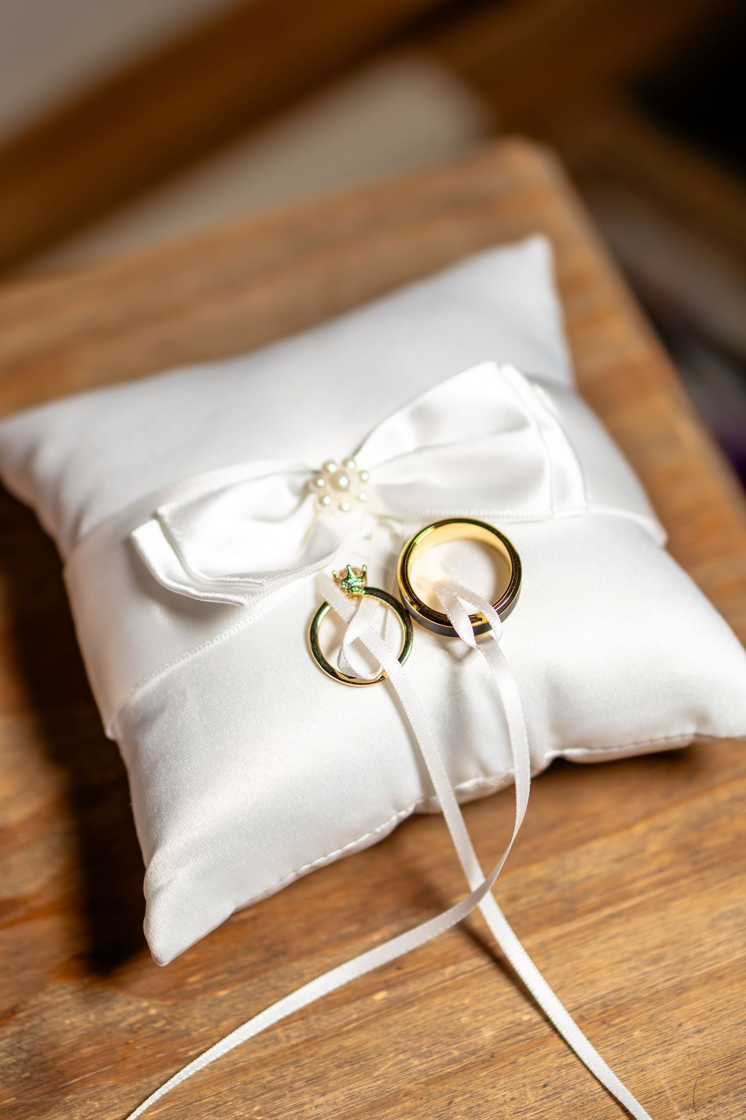 Two gold wedding rings tied with white ribbon rest elegantly on a white satin ring bearer pillow.