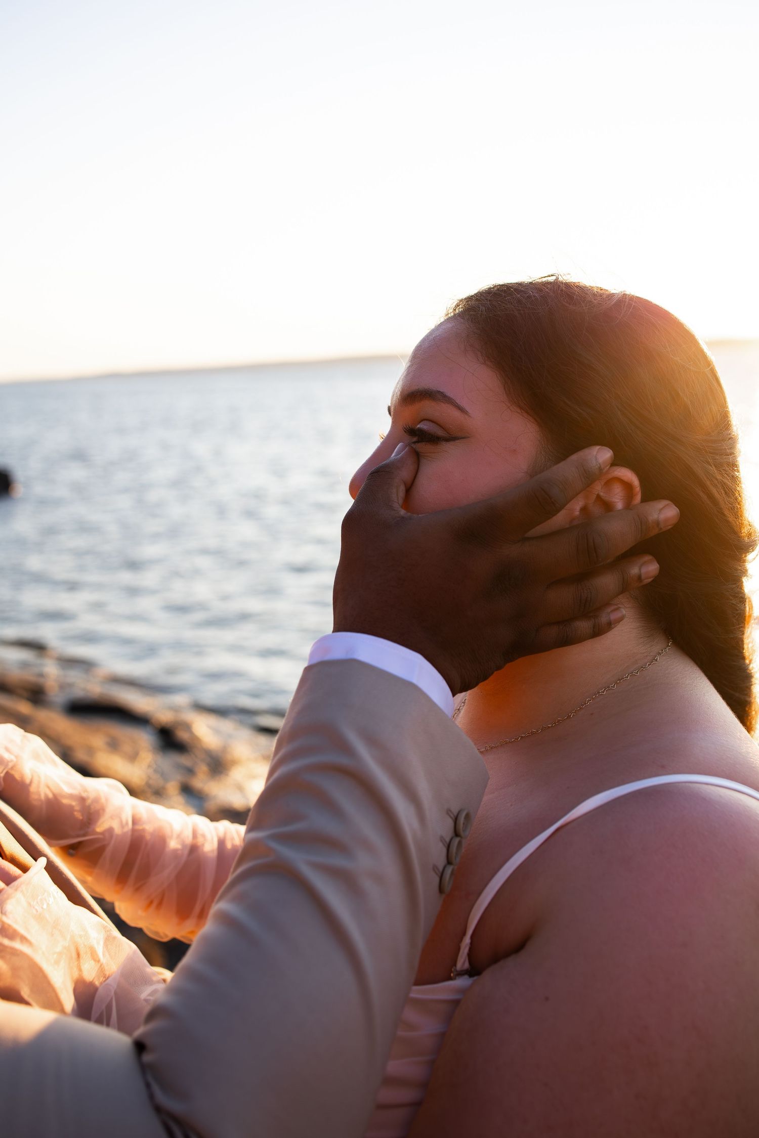 Couple sharing a romantic moment at sunset by the ocean, with golden light illuminating their tender embrace.