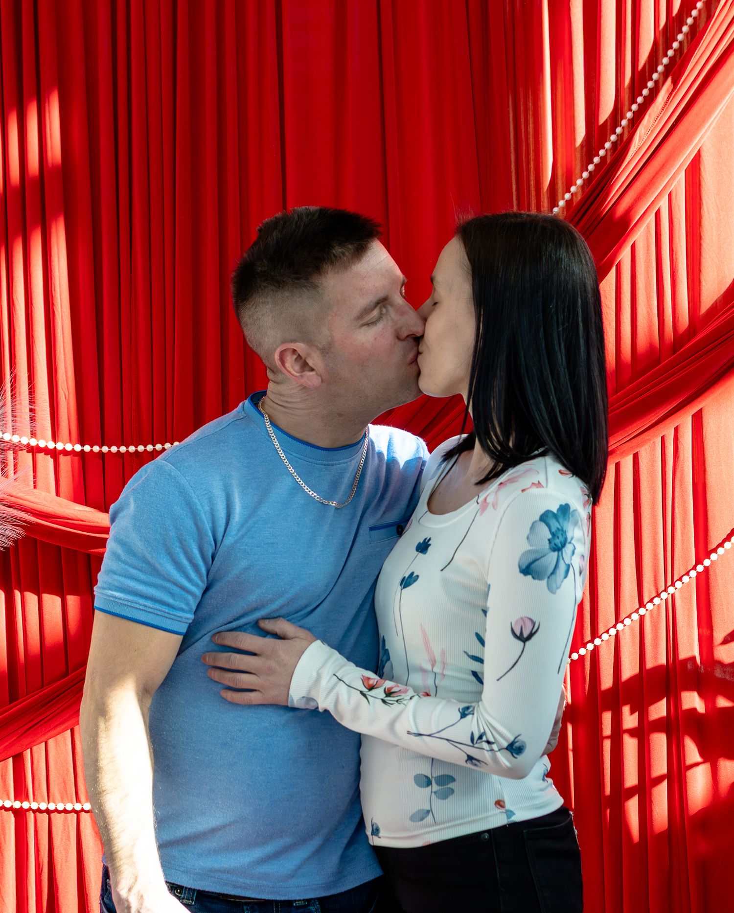 Couple sharing a romantic kiss in front of a vibrant red draped curtain background.