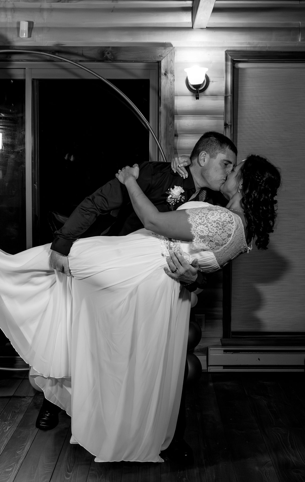 Black and white romantic dip kiss between bride in white gown and groom at wedding reception.