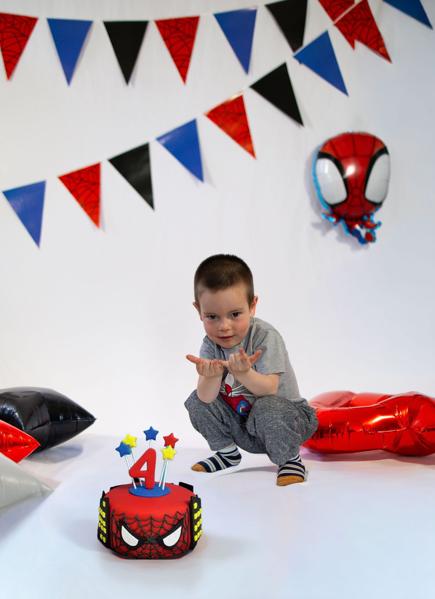 Boy clapping at Spiderman themed 4th birthday with cake, balloons, and bunting decorations on white background.