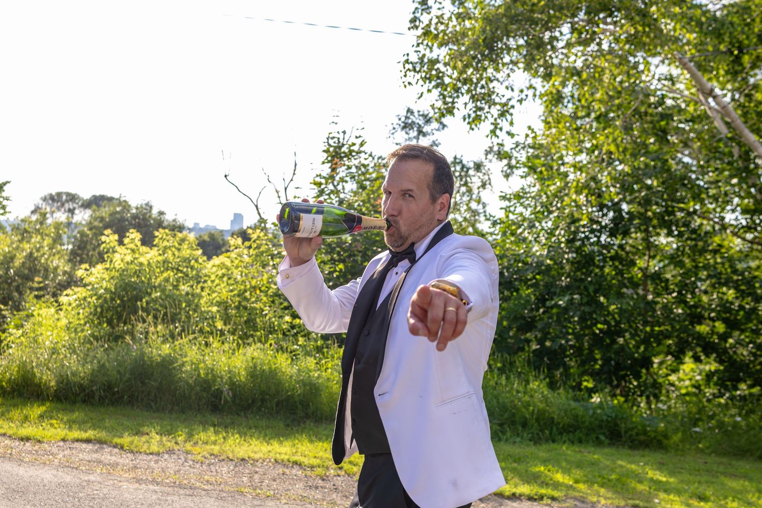 Man in white shirt and tie pouring champagne outdoors at a celebration event.
