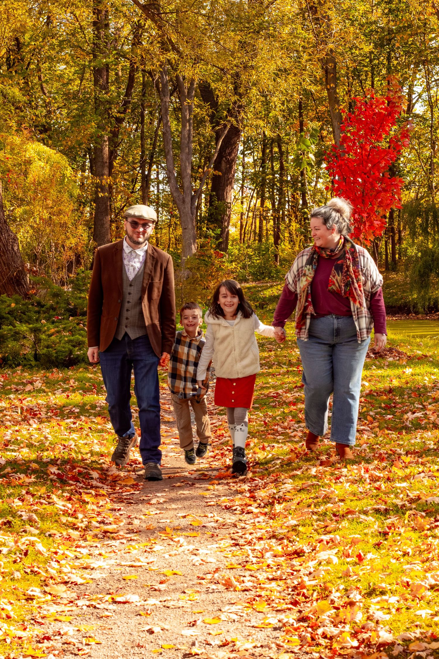 Family of four walking together on a leaf-covered path in a colorful autumn park.