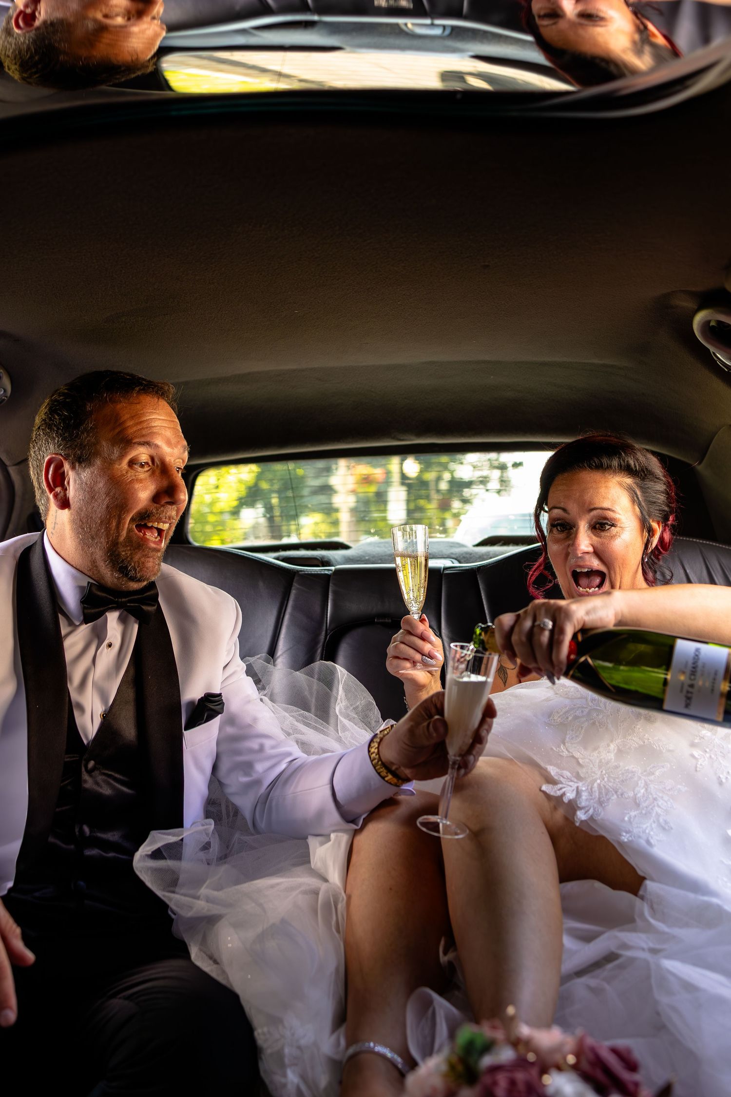 Newlyweds celebrating in a limousine, toasting with champagne glasses, bride in white gown and groom in tuxedo.