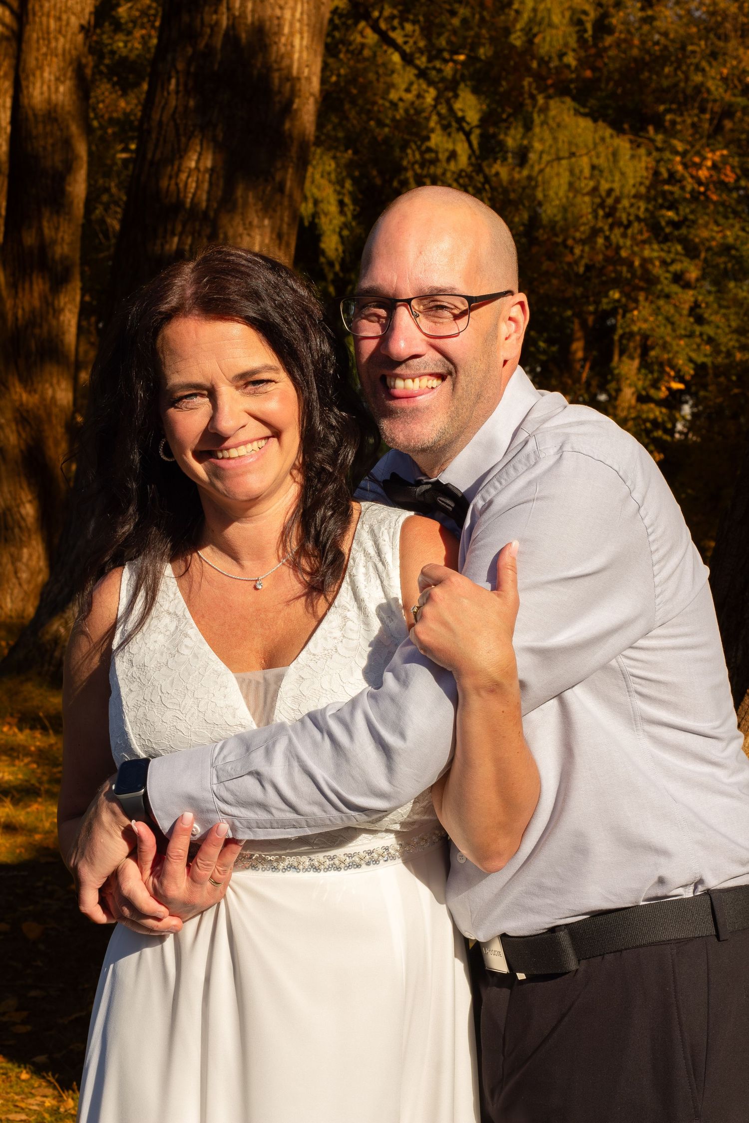 Smiling couple embracing warmly in golden autumn light among tall trees.