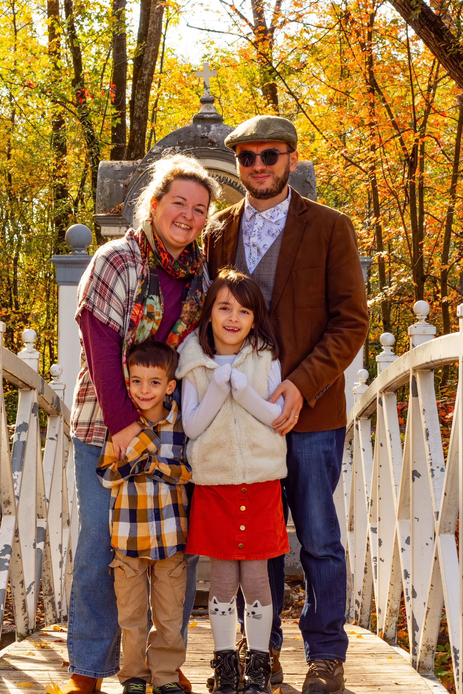 Happy family of four posing on a white bridge surrounded by vibrant autumn foliage.