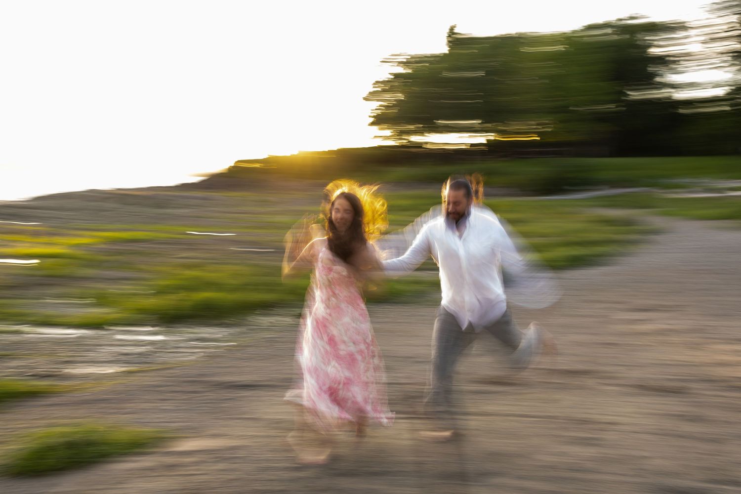 A couple joyfully runs hand-in-hand at sunset, motion blur capturing their energy in a romantic outdoor setting.