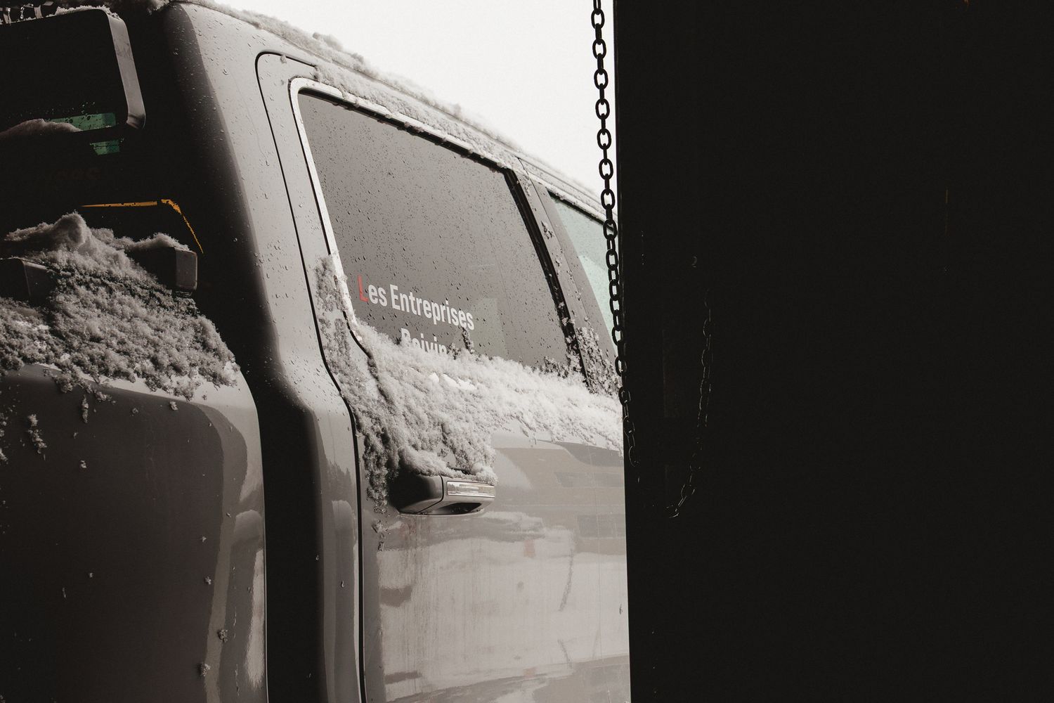 Snow-covered dark vehicle door with a white sticker visible in a winter setting.