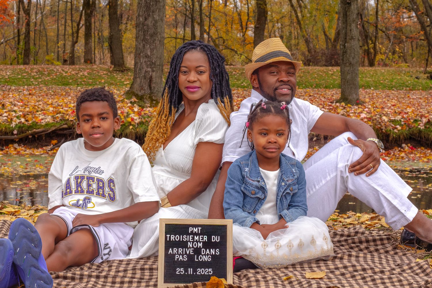 African American family sitting on a blanket in autumn park holding a chalkboard pregnancy announcement sign.