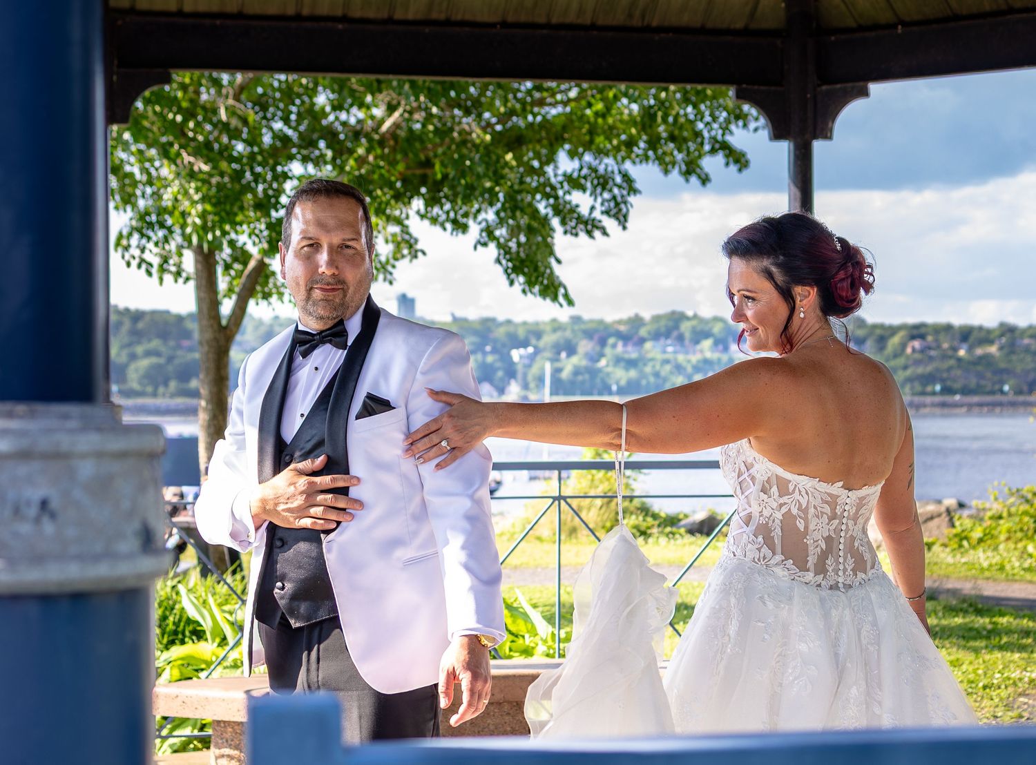 Bride taps groom's shoulder during outdoor first look moment at waterfront gazebo wedding venue.