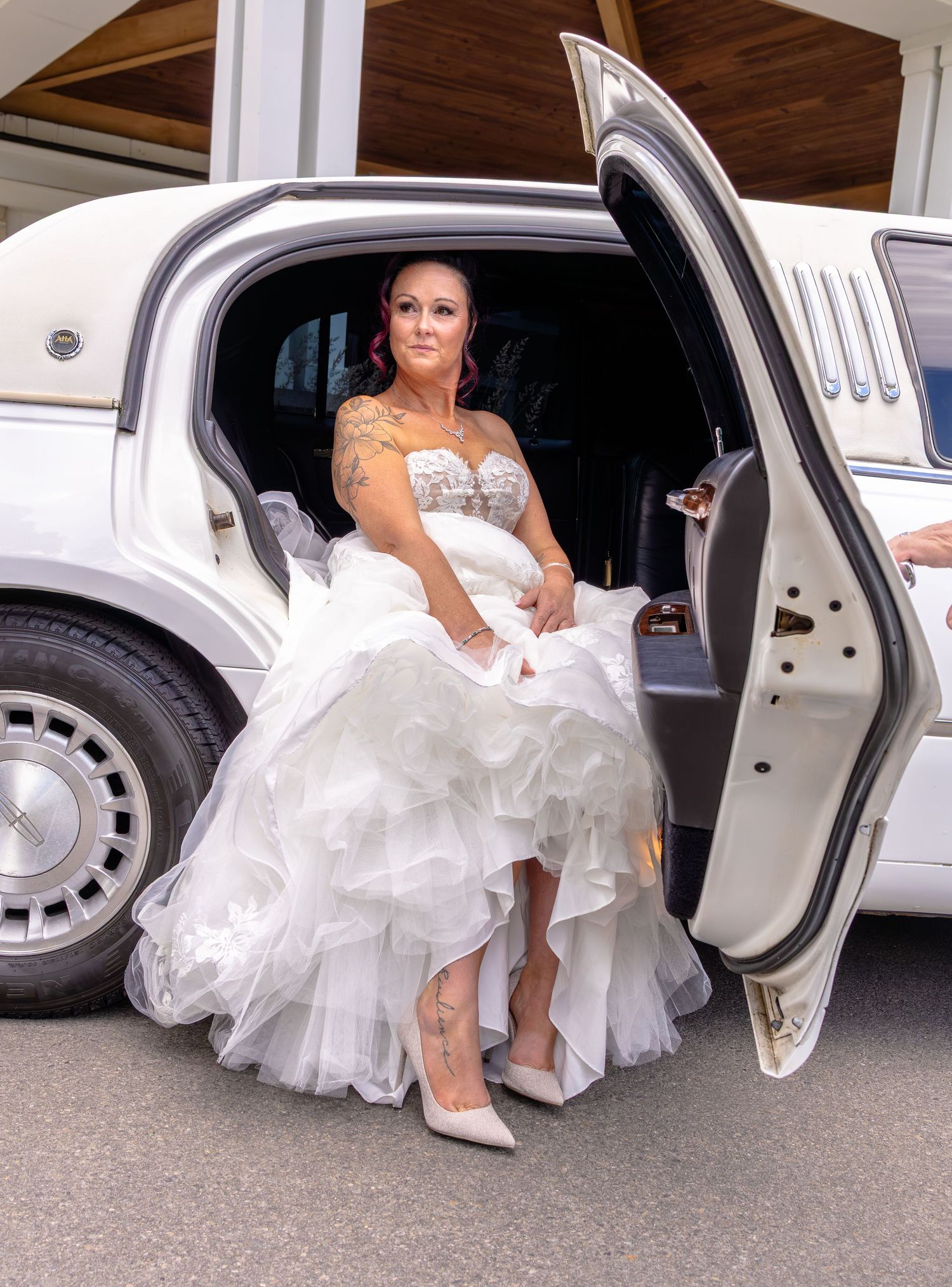 Bride in white ruffled gown and heels stepping out of a white limousine on her wedding day.