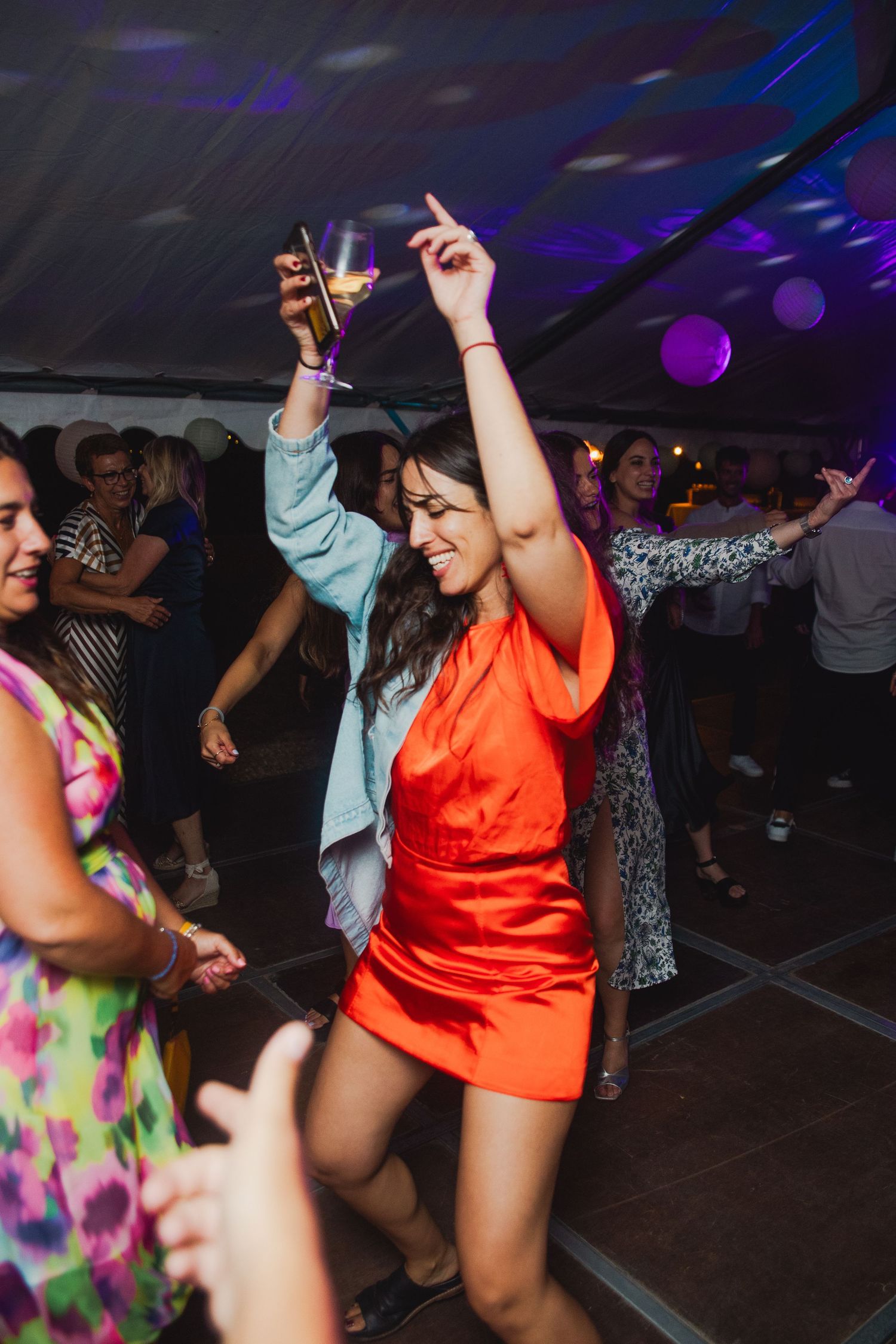 Party guests dancing and socializing on a dark dance floor with purple lighting and disco atmosphere at night.