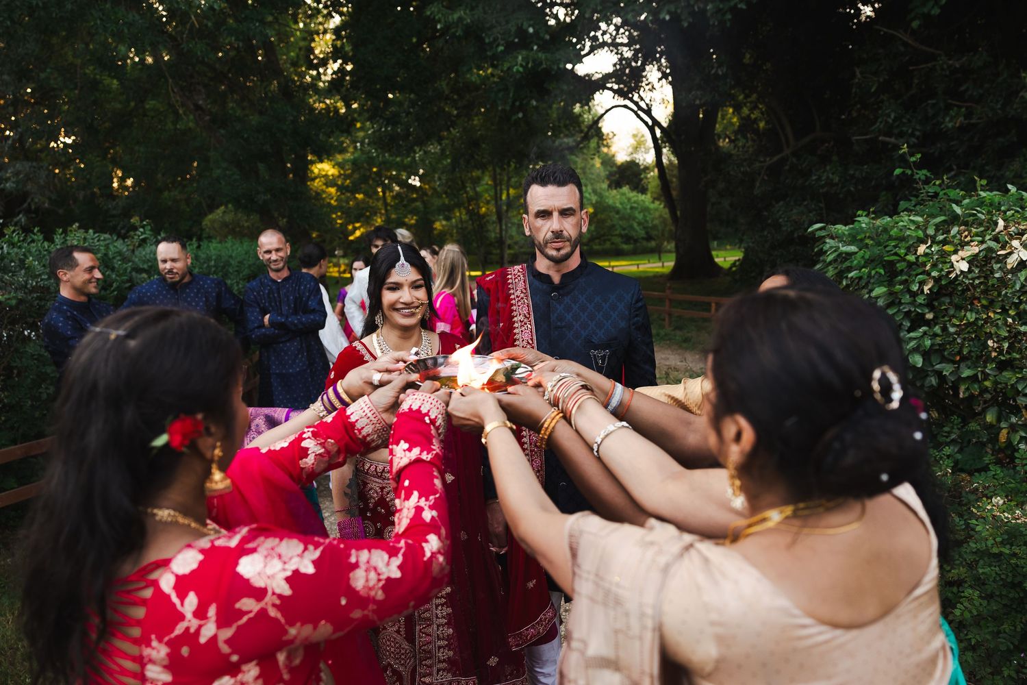 Traditional Indian wedding guests performing energetic dance moves in a garden with red saris and vibrant colors.