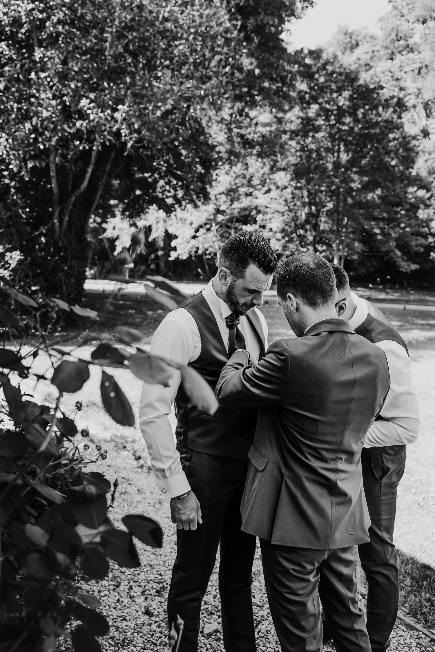 A group in formal attire gathers playfully outside in a garden setting creating candid black and white moments.