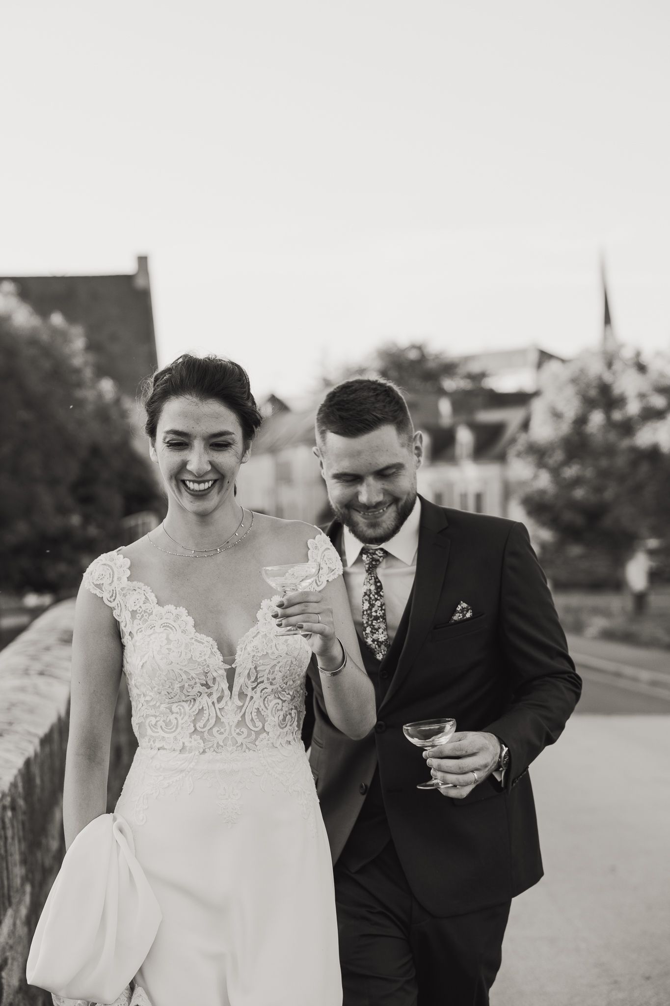 A joyful couple in wedding attire laughing together while walking outdoors in black and white.