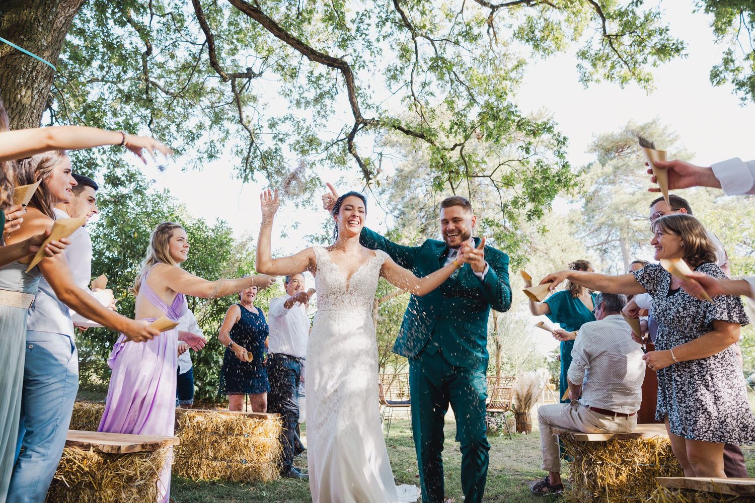 Wedding party dances together in a rustic outdoor setting during a joyful celebration on a sunny day.