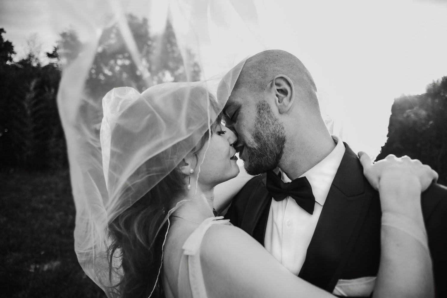 Intimate black and white portrait of couple sharing romantic moment under bride's veil.