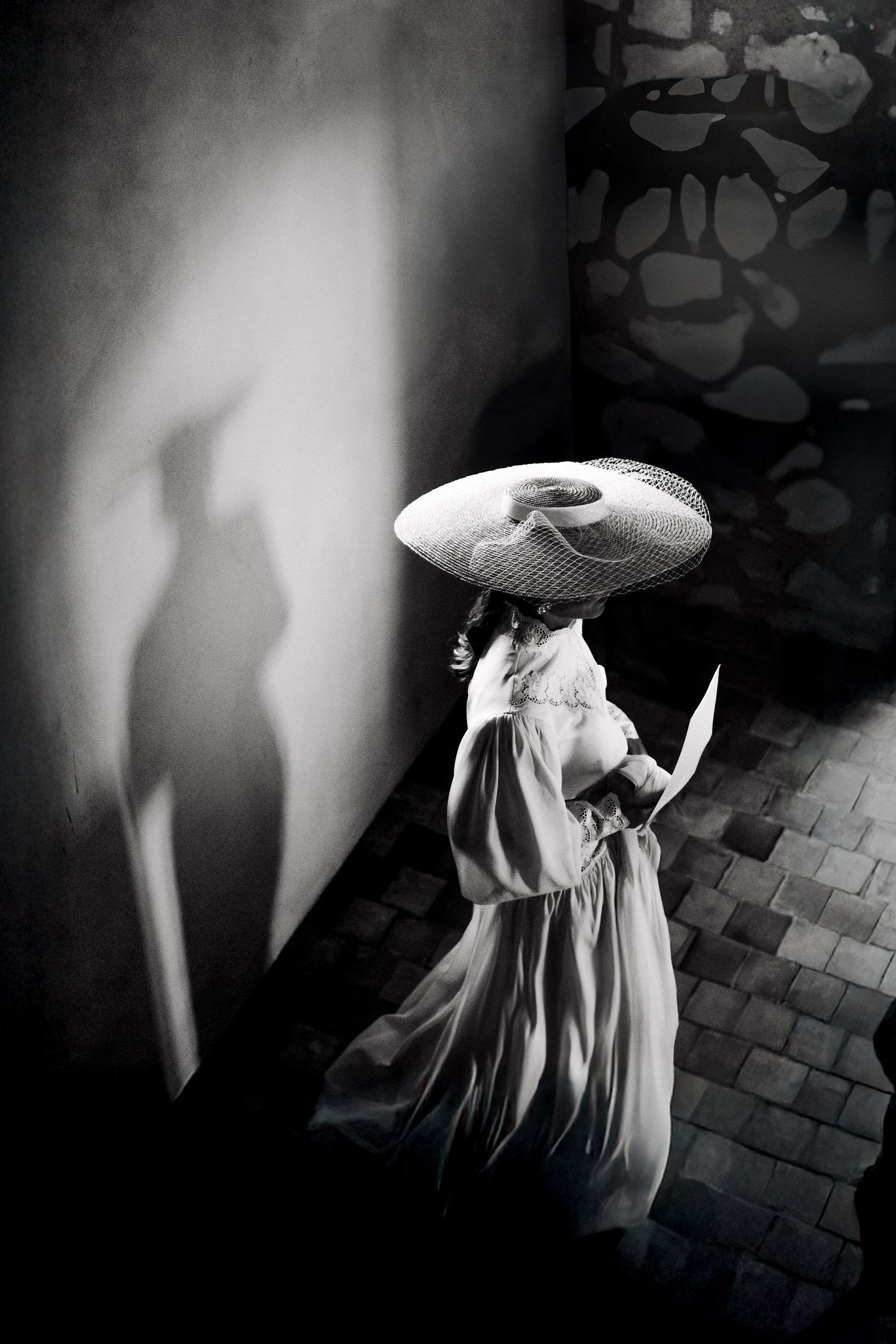 A black and white composite image shows multiple angles of a person in a flowing white dress on a dark cobblestone background.
