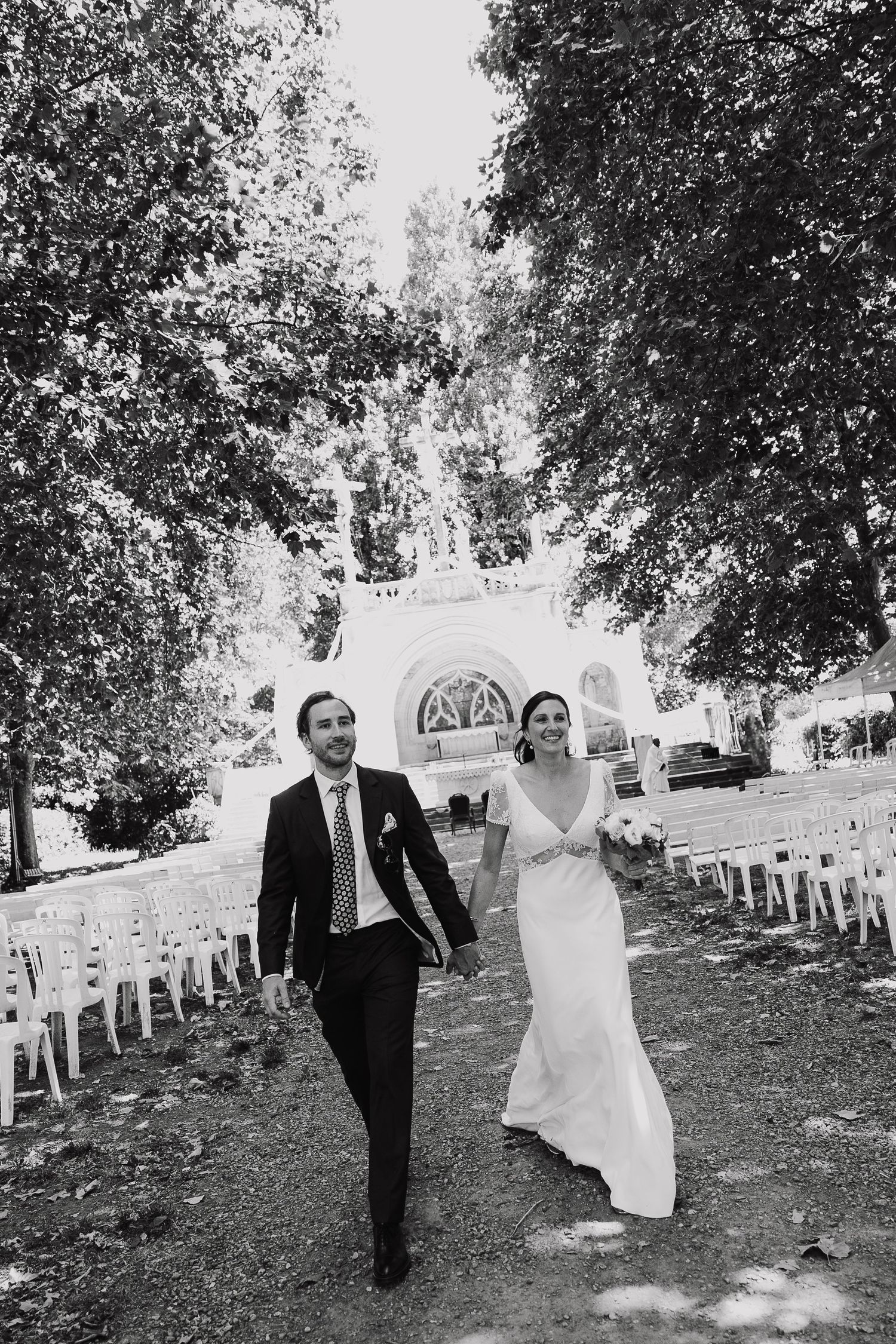 Black and white photo of a smiling bride and groom walking down the aisle after their outdoor wedding ceremony.