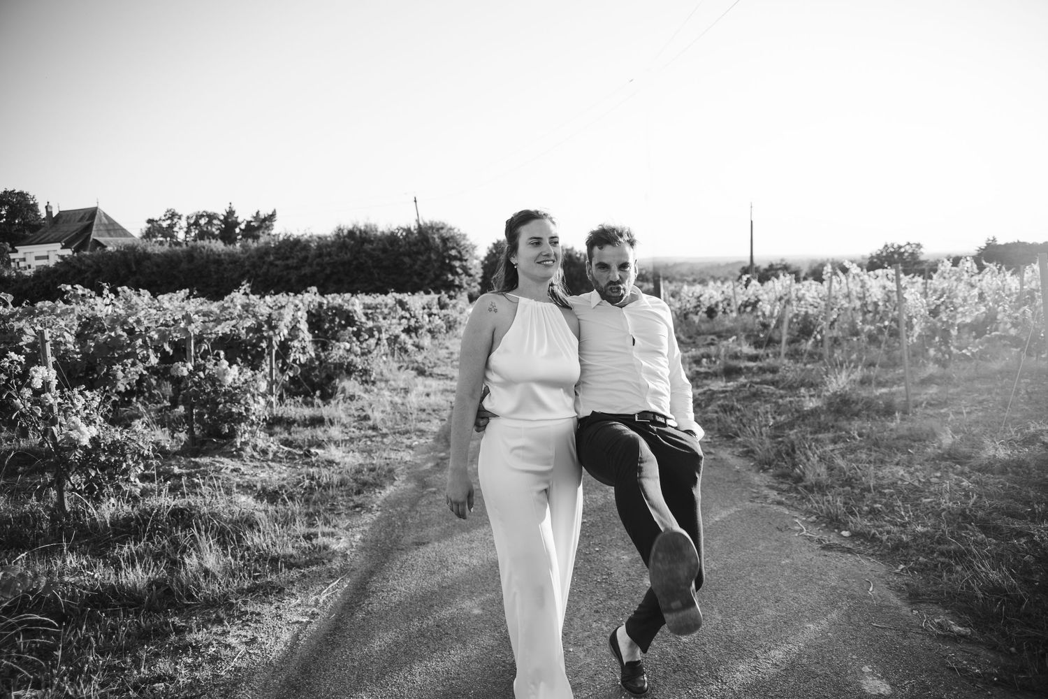 Black and white photo of a couple walking hand in hand down a rural path surrounded by lush fields.