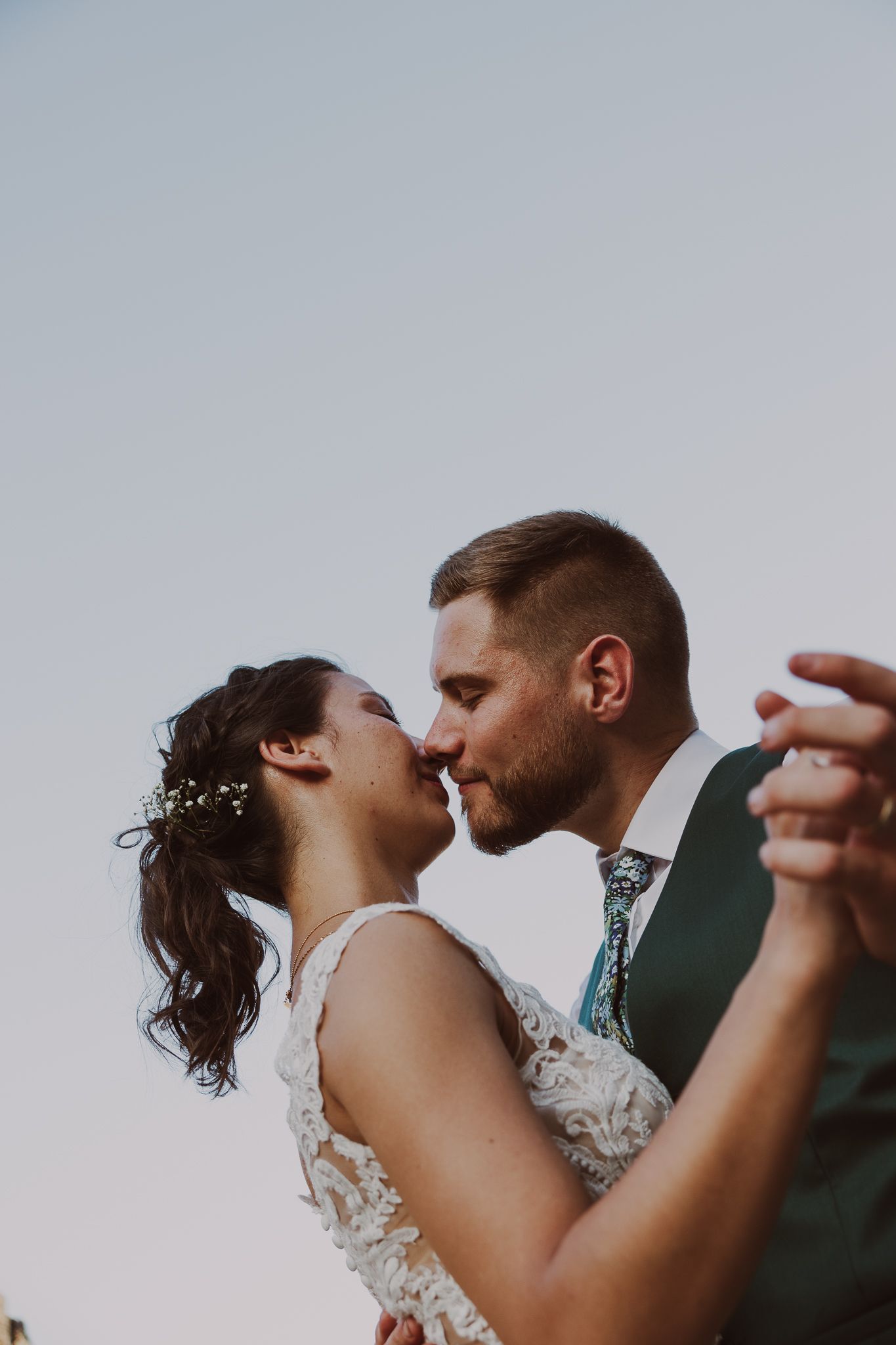 A couple shares an intimate dance moment at sunset with the bride wearing a lace dress and groom in dark suit.