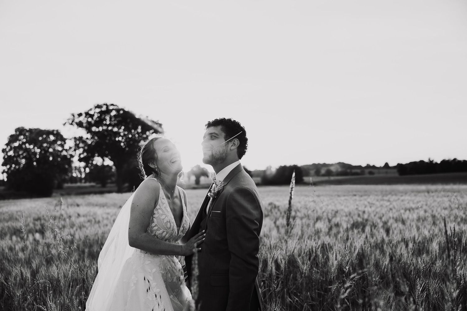 A couple kisses in a wheat field at sunset, captured in dramatic black and white photography.