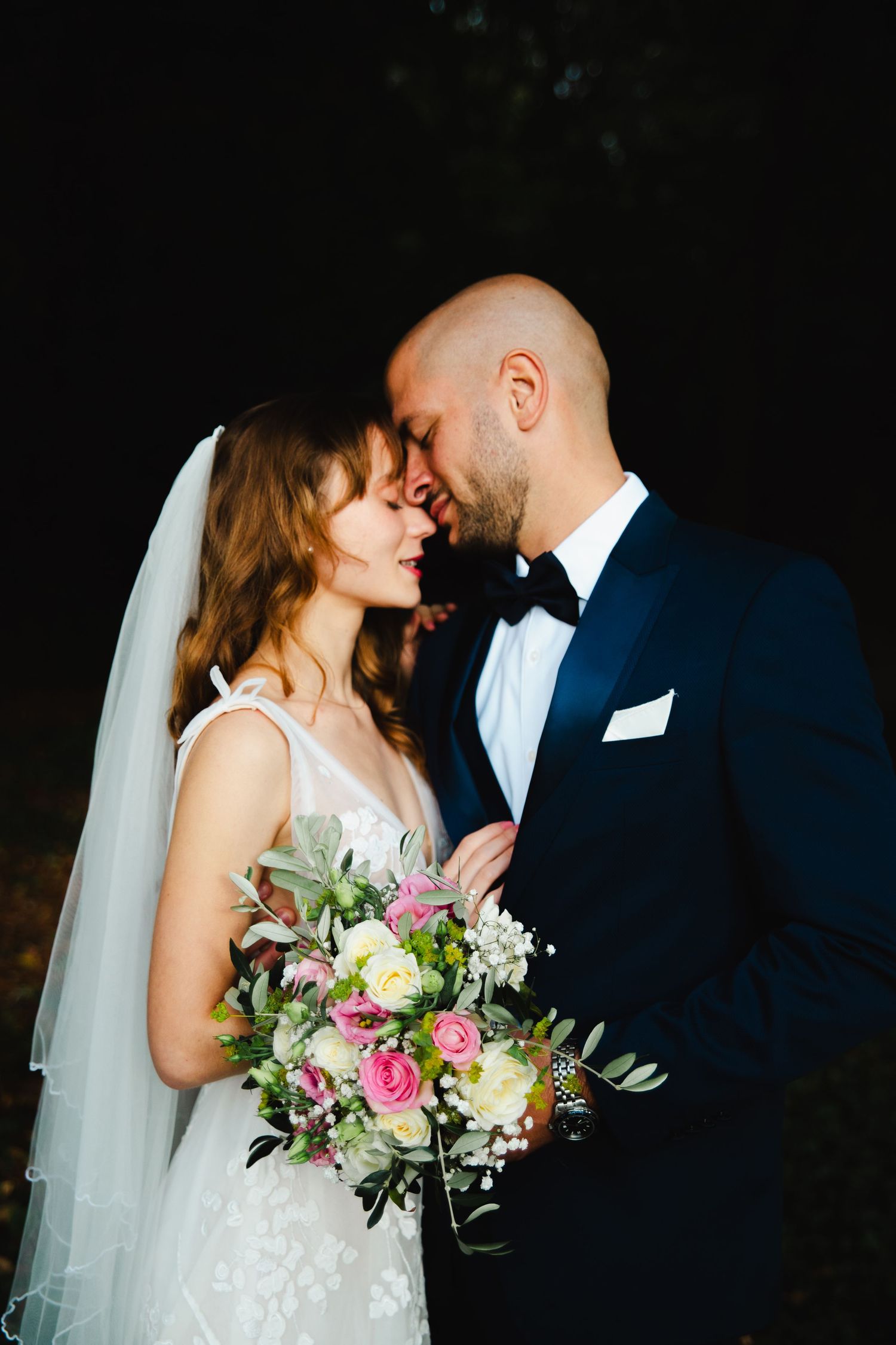 Romantic wedding portrait showing couple in tender moment with bride holding beautiful pink and white floral bouquet.