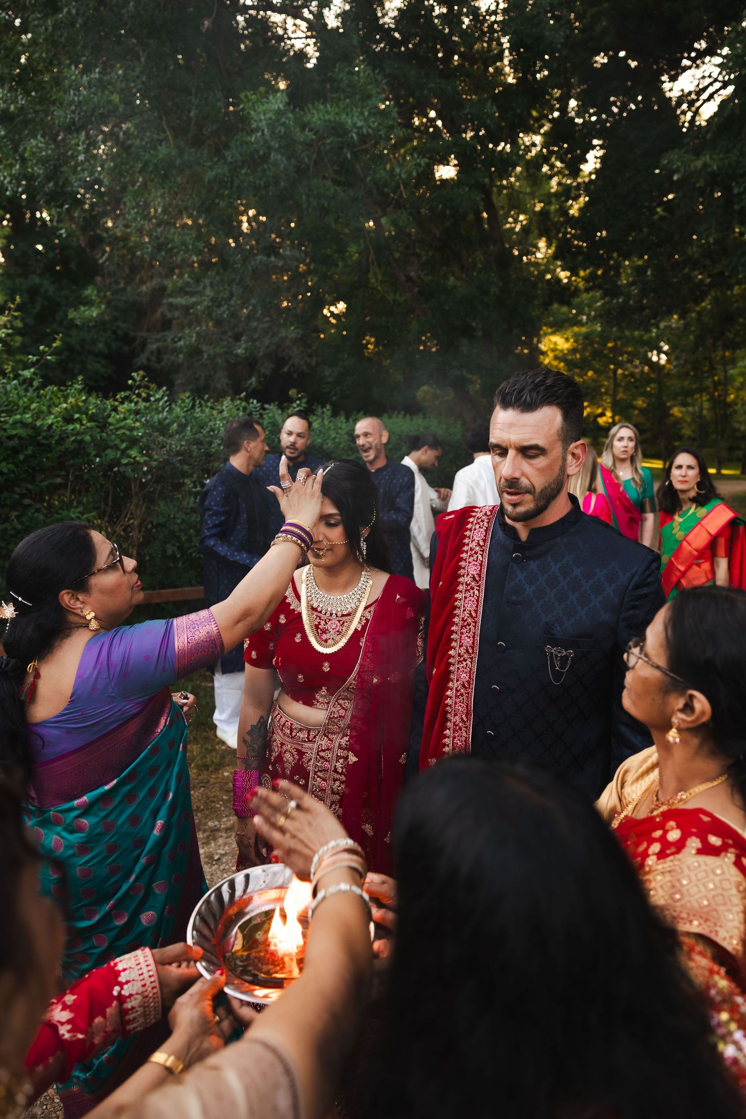 Traditional Indian wedding ceremony guests participate in cultural ritual with burning flame offerings outdoors at dusk.