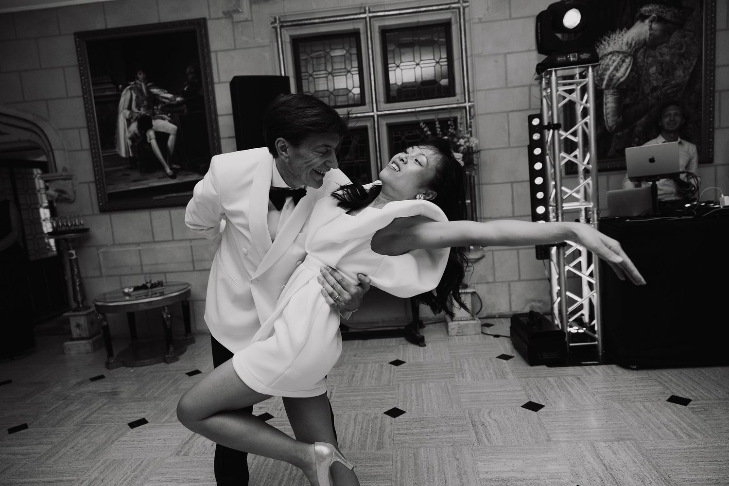 Couple dancing elegantly in black and white photo at a wedding reception with DJ setup in background.