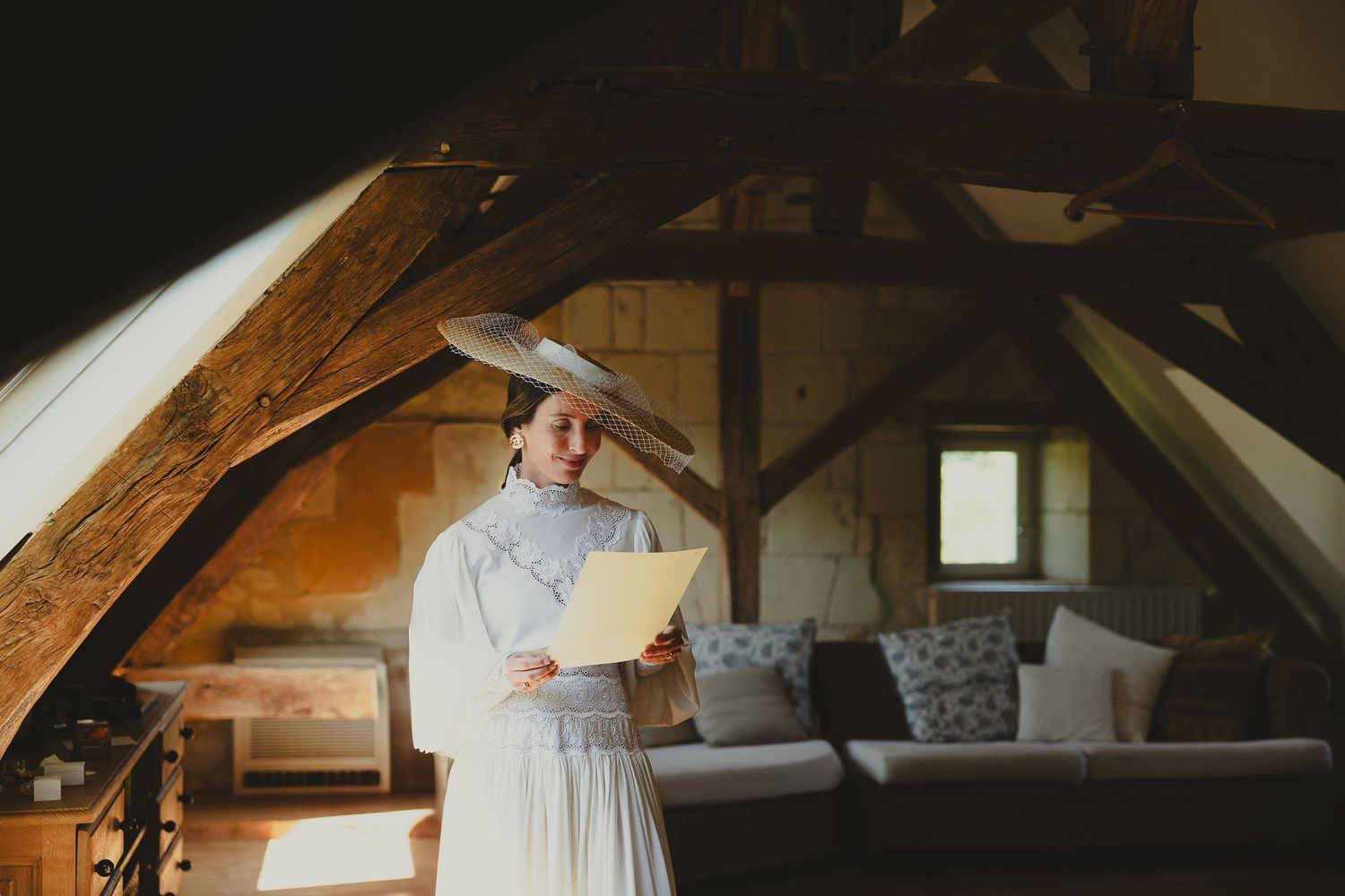 Someone wearing a white dress stands in a cozy wooden attic loft with exposed beams and natural light streaming in.