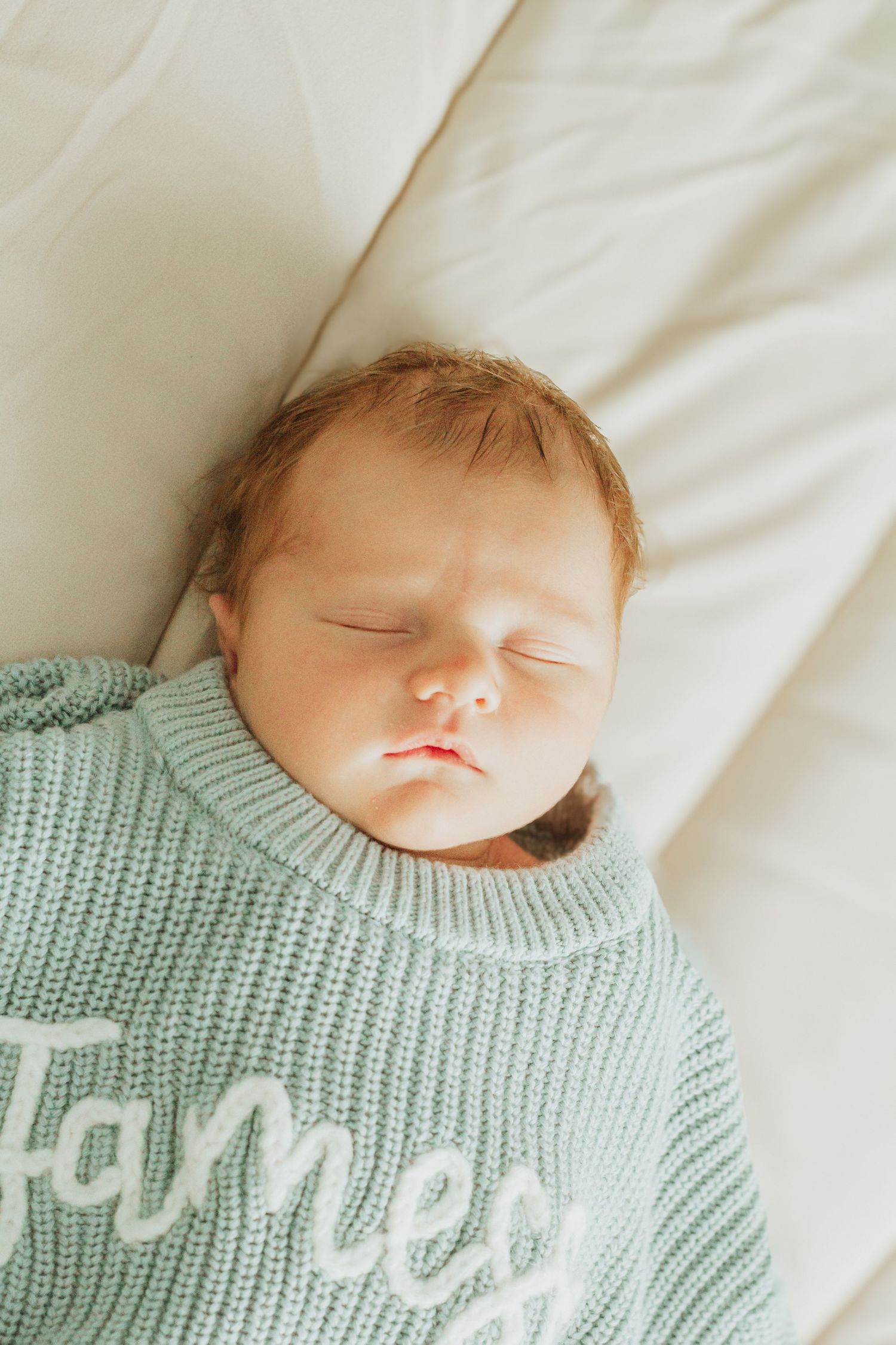 Sleeping newborn baby wrapped in a mint green knit blanket personalized with the name James.