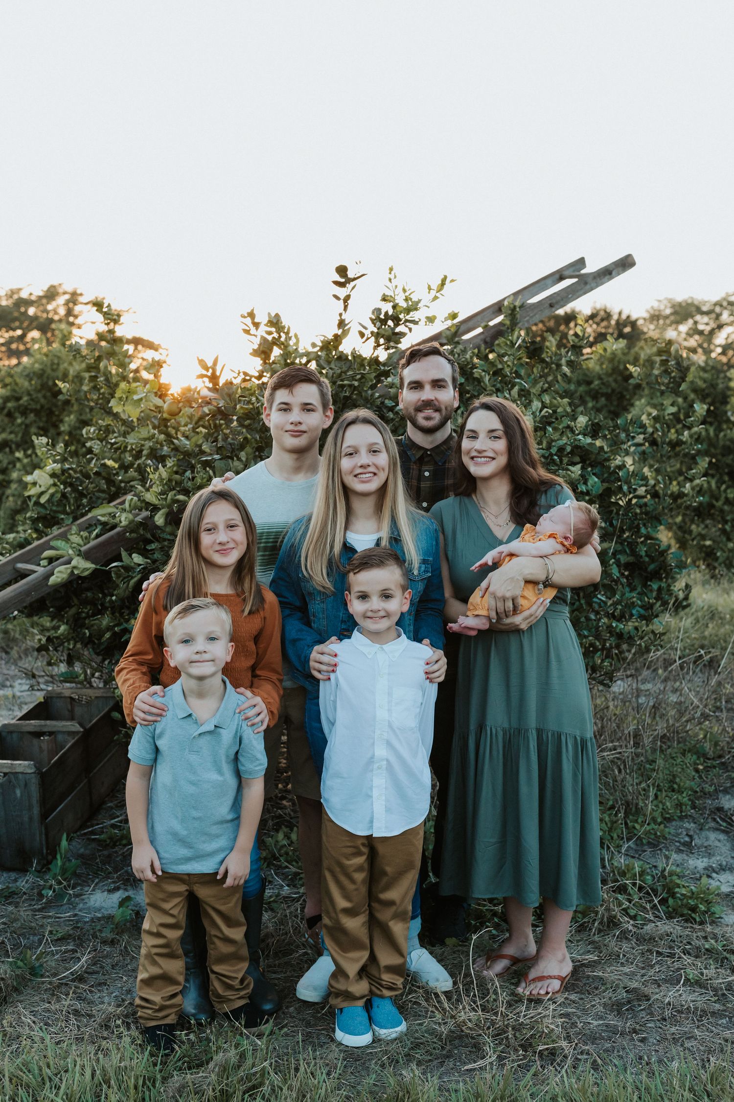 Family portrait at sunset with children in light blue shirts and adults in earth-toned clothing.