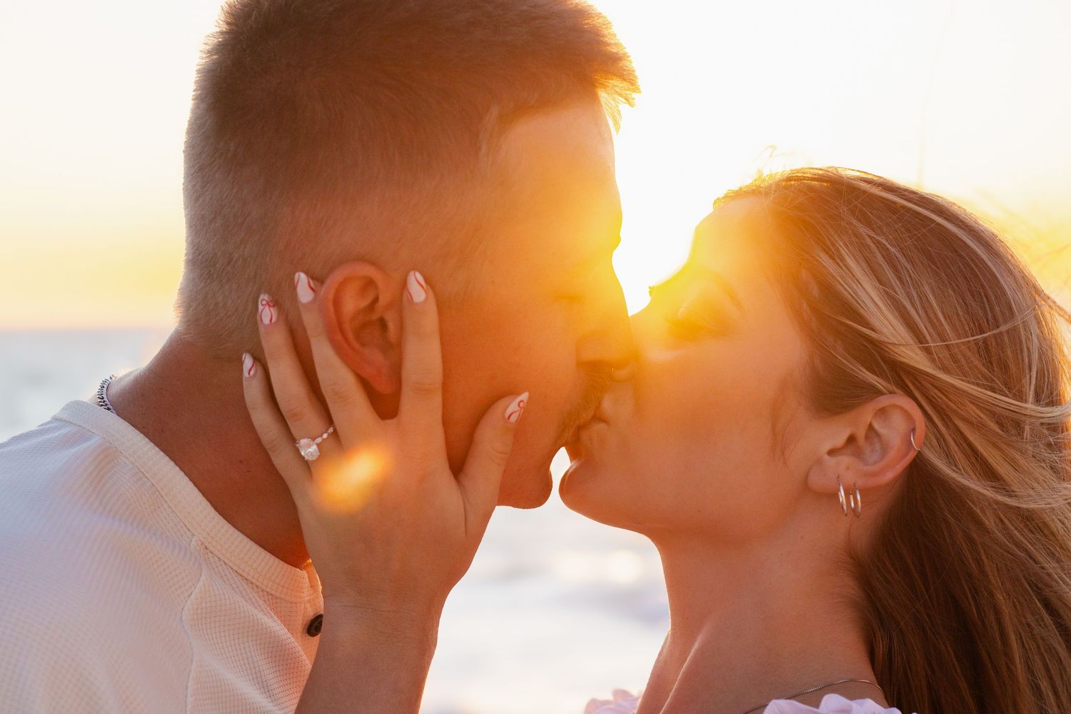 Couple sharing a romantic kiss at golden sunset by the beach, warm sunlight glowing behind them.