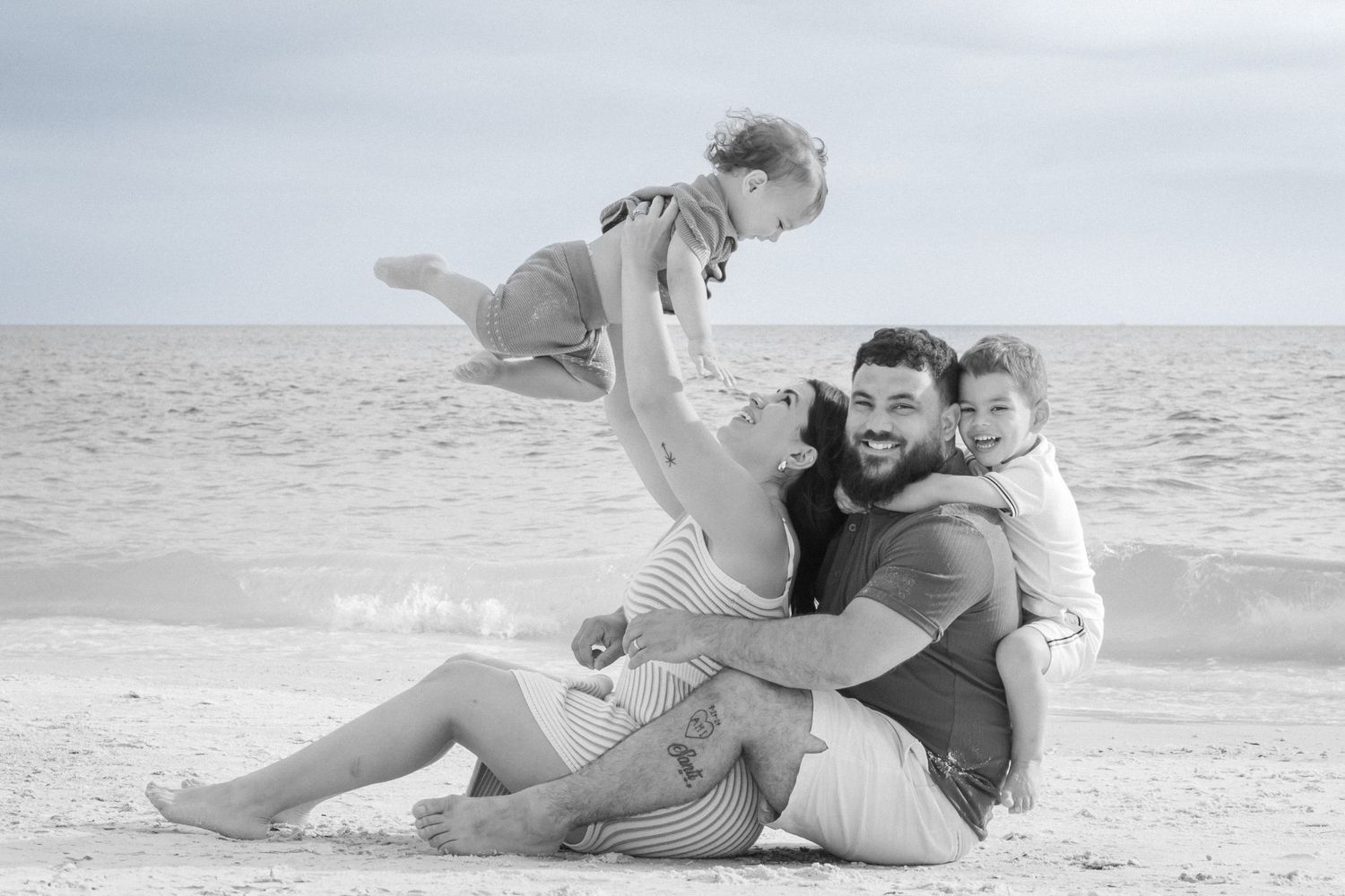Black and white photo of a happy family playing on the beach, father lifting child in the air.