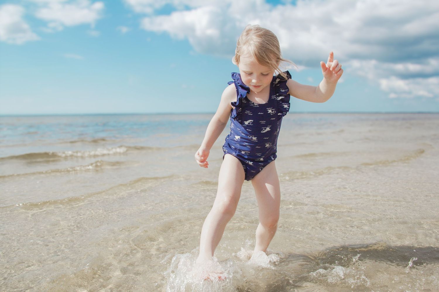 Child splashing in ocean waves at the beach wearing a navy blue swimsuit.