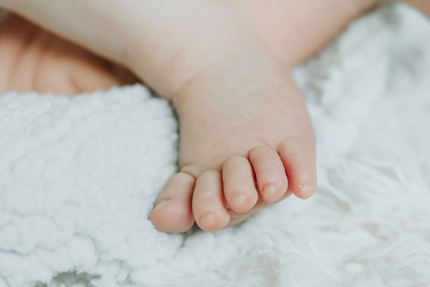 Close-up of a newborn baby's tiny foot resting on a soft white blanket.