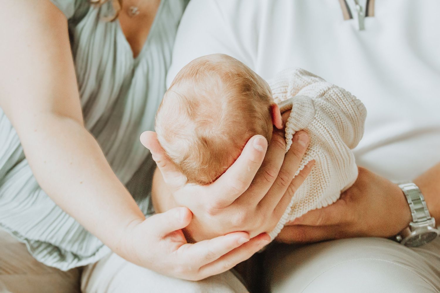 Parents tenderly cradling their newborn baby, with gentle hands supporting the infant's head in a warm, loving embrace.