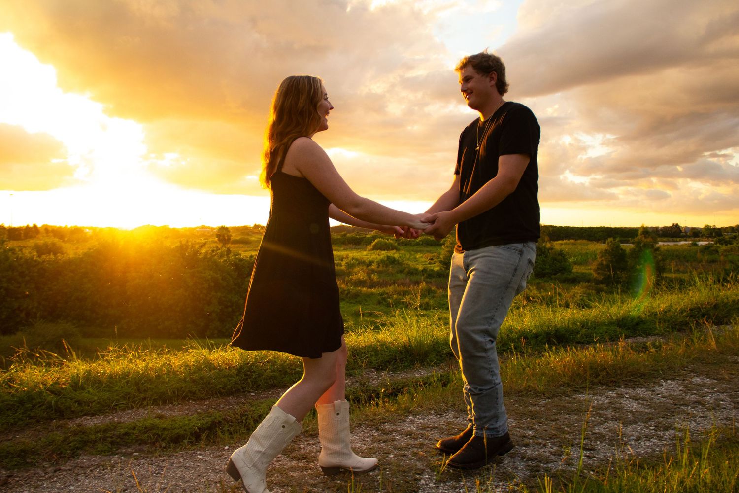 Couple holding hands facing each other on a path during a vibrant golden sunset.
