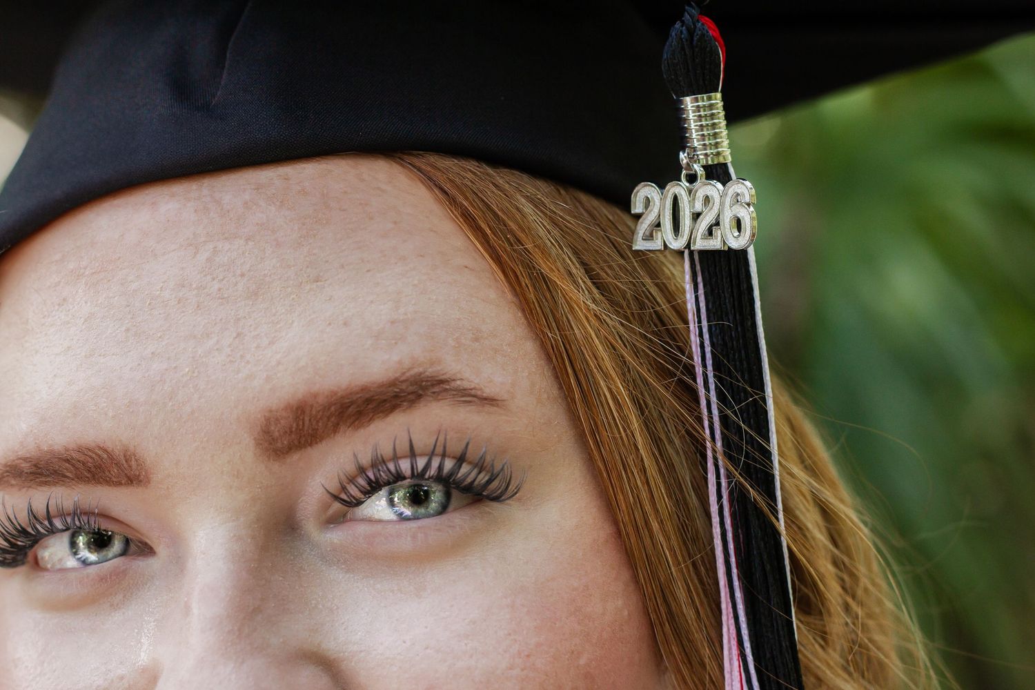 Close-up of a redhead woman wearing a black graduation cap with a 2025 tassel, showcasing green eyes.