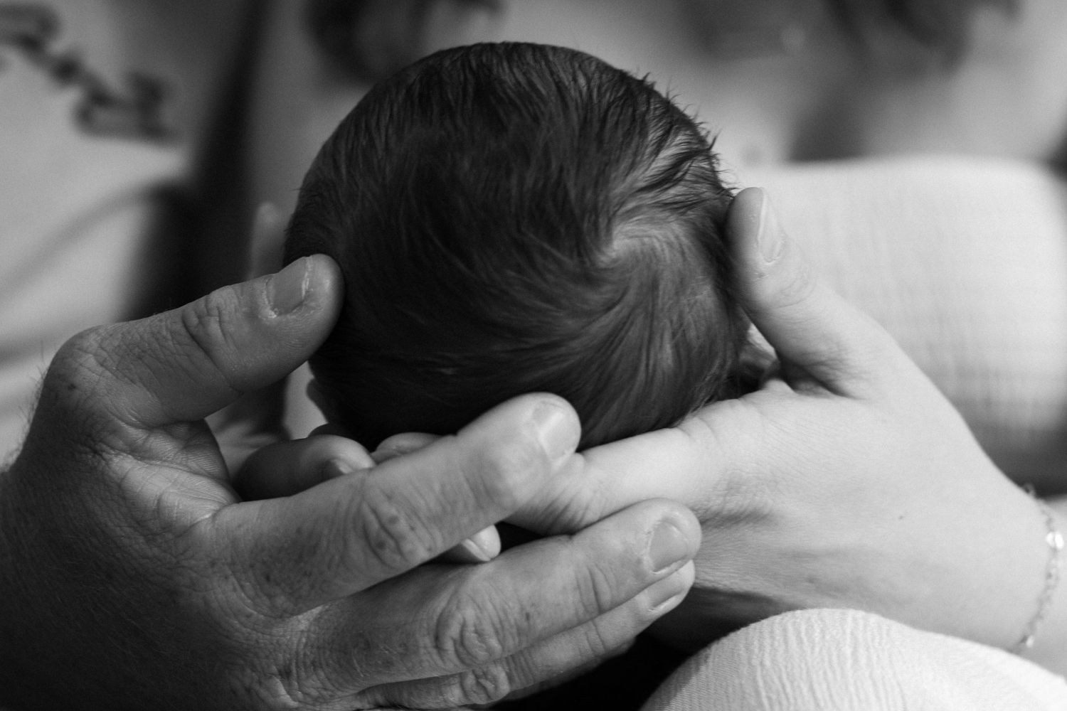 Black and white photo of a newborn baby cradled gently in adult hands, symbolizing new life and parental love.