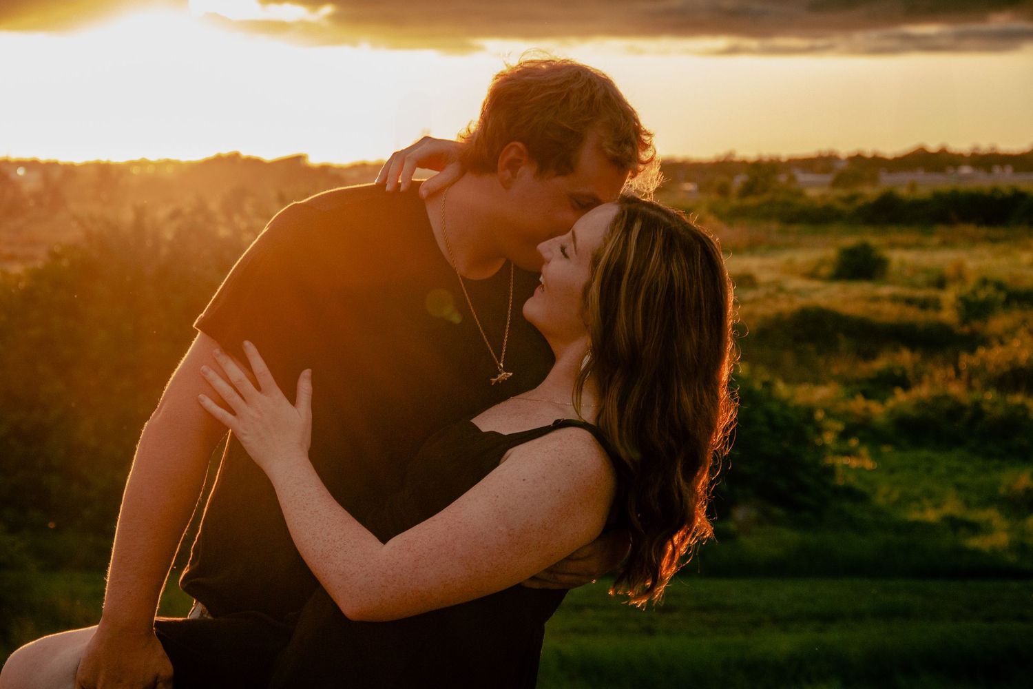Romantic couple sharing a kiss outdoors during a warm golden sunset.