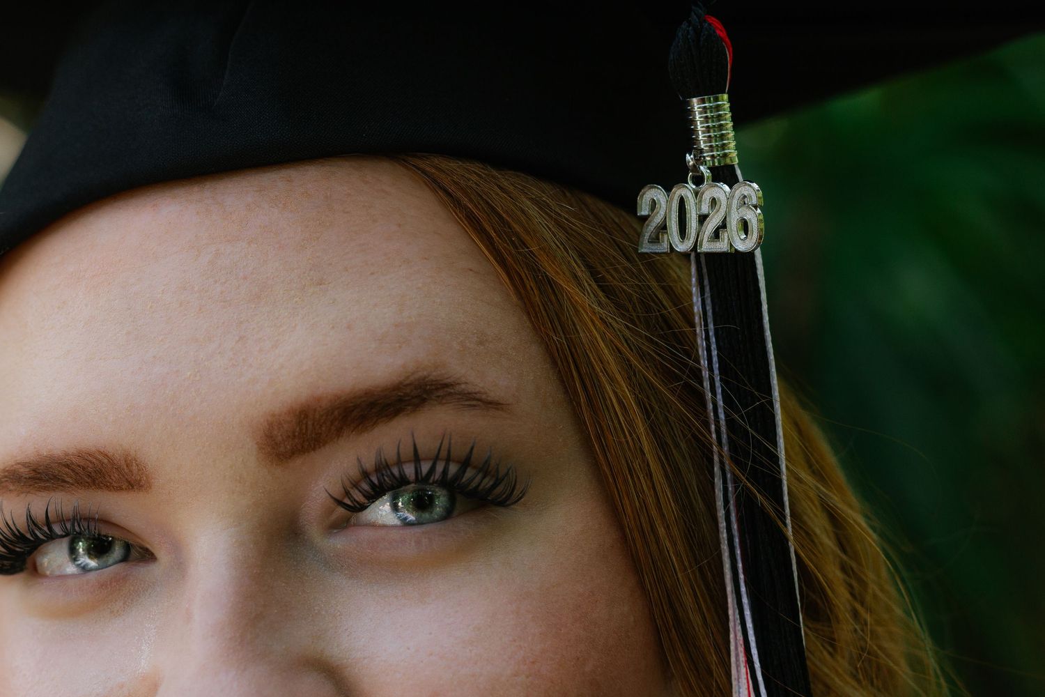 Close-up of a young woman wearing a black graduation cap with a 2025 tassel, showcasing bright green eyes.