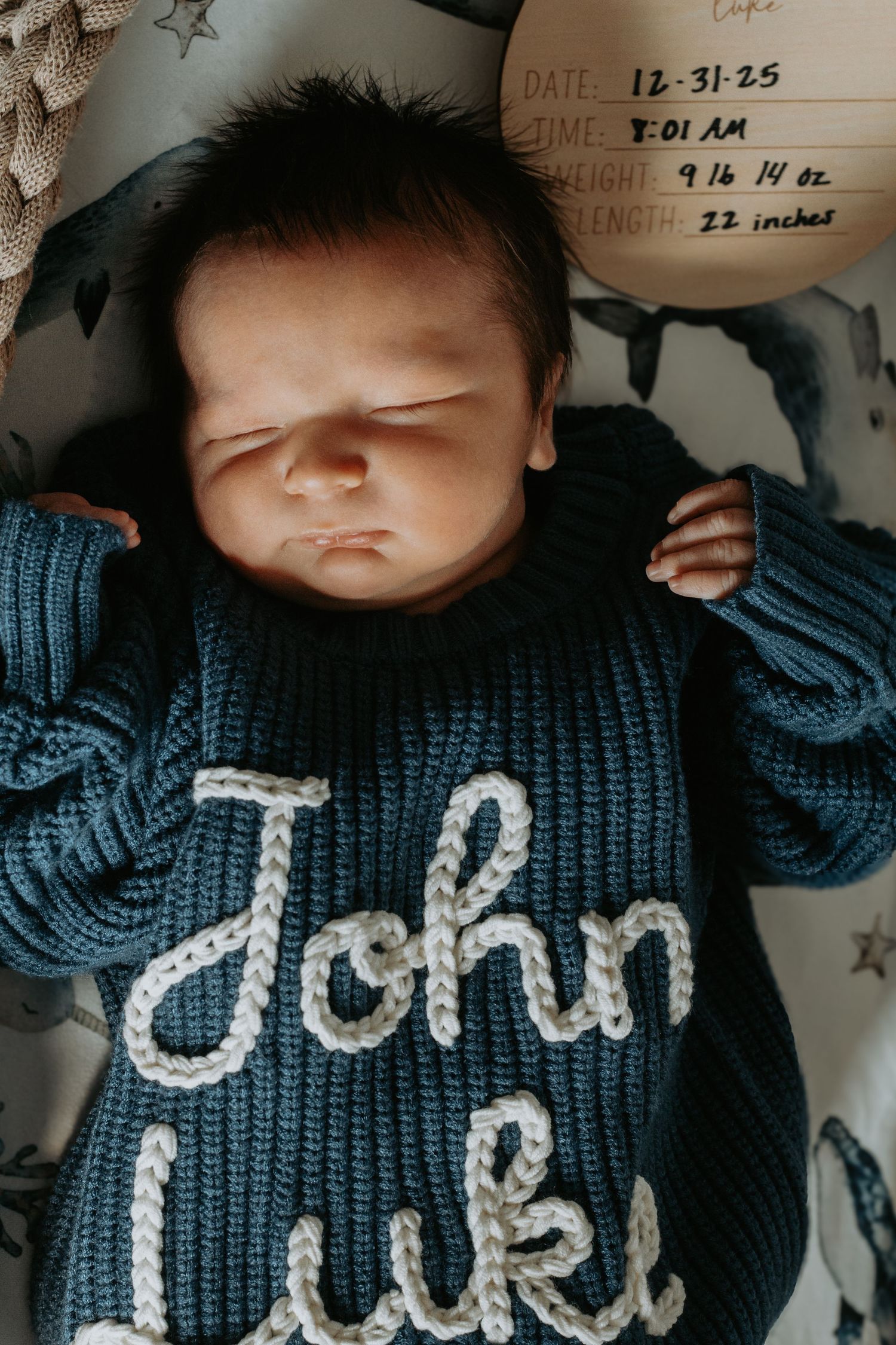 A baby wearing a navy blue knit sweater with white lettering lies on their back against a light background.